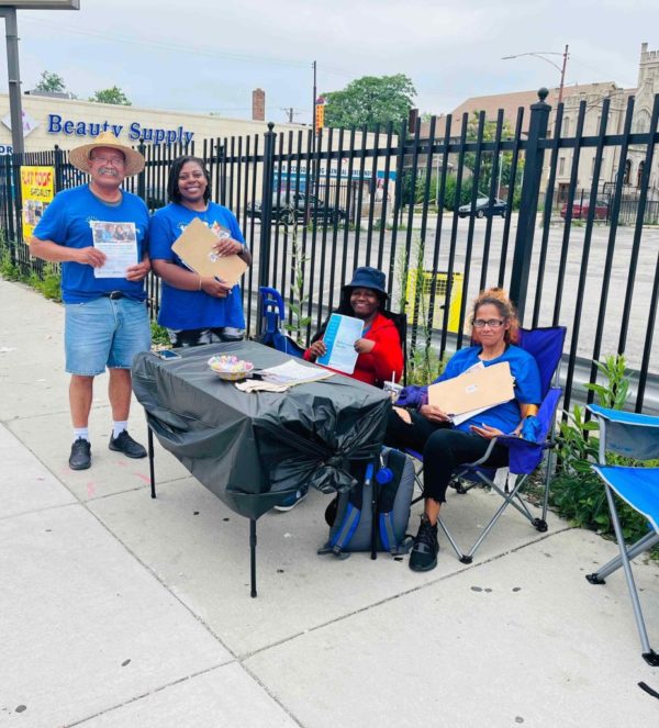 Four parent leaders, two are standing and two are sitting. They are by a table doing outreach in the community.