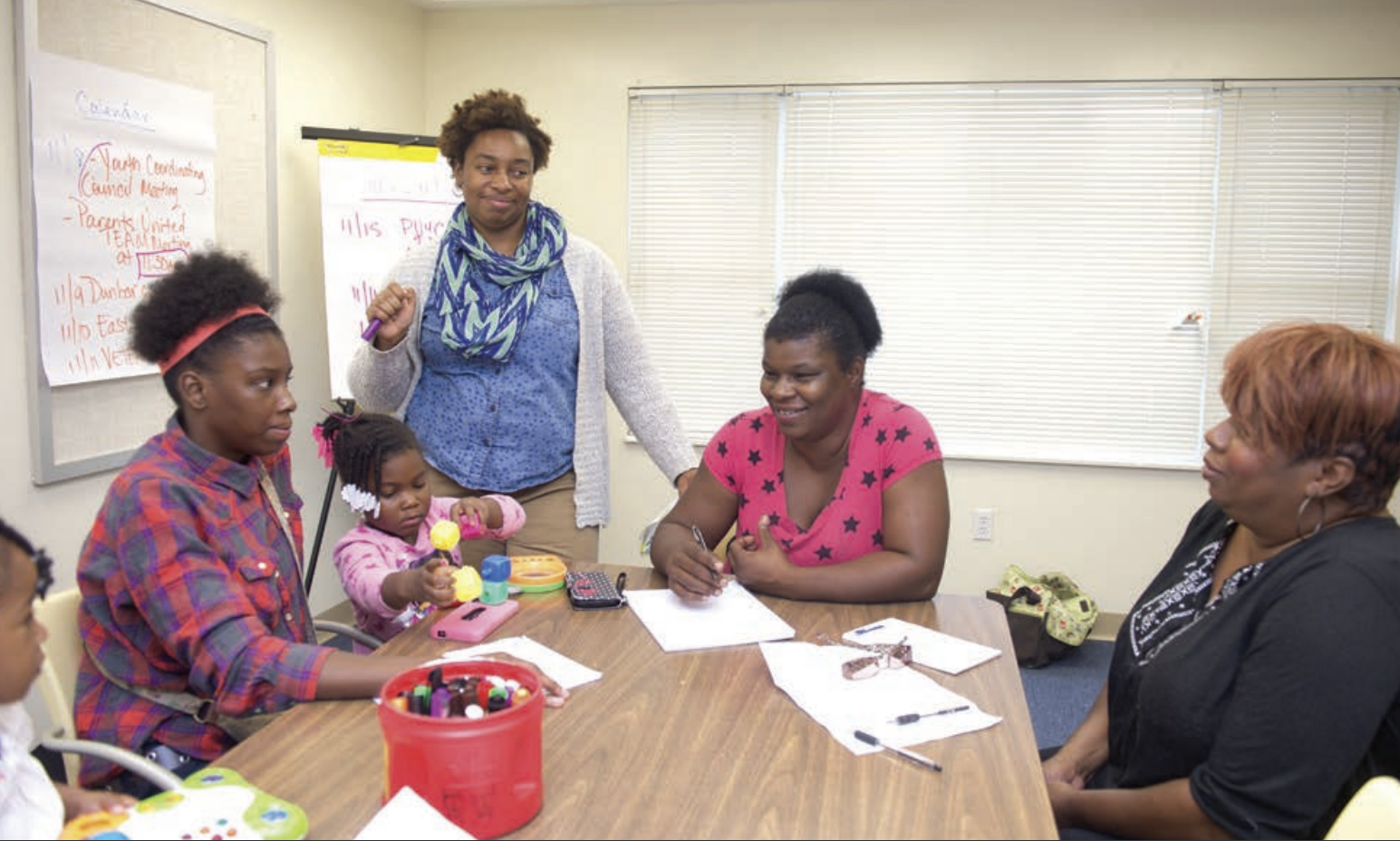 A COFI organizer stands next to a group of mothers and their children in a classroom