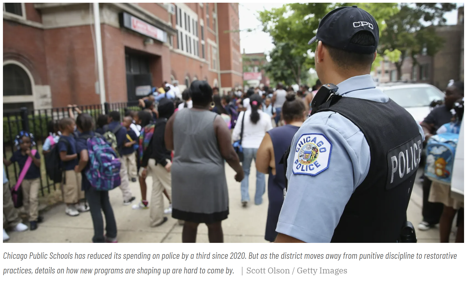 Una imagen de captura de pantalla de un policía afuera de una escuela primaria con muchos niños afuera; Crédito de la imagen: Scott Olson.