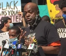 Un hombre afroamericano se para frente a varios micrófonos durante una conferencia de prensa.
