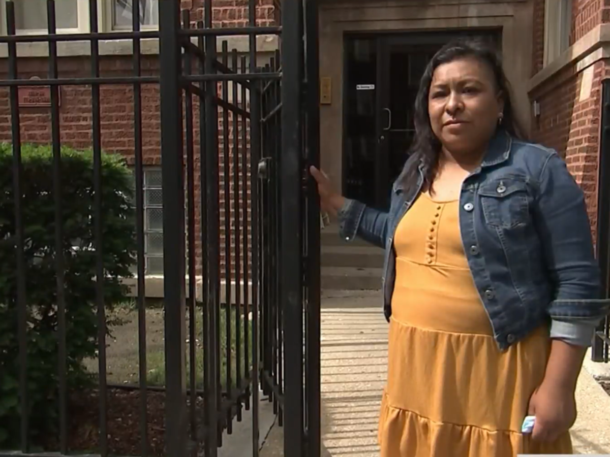 A Latina mother stands in front of a gate