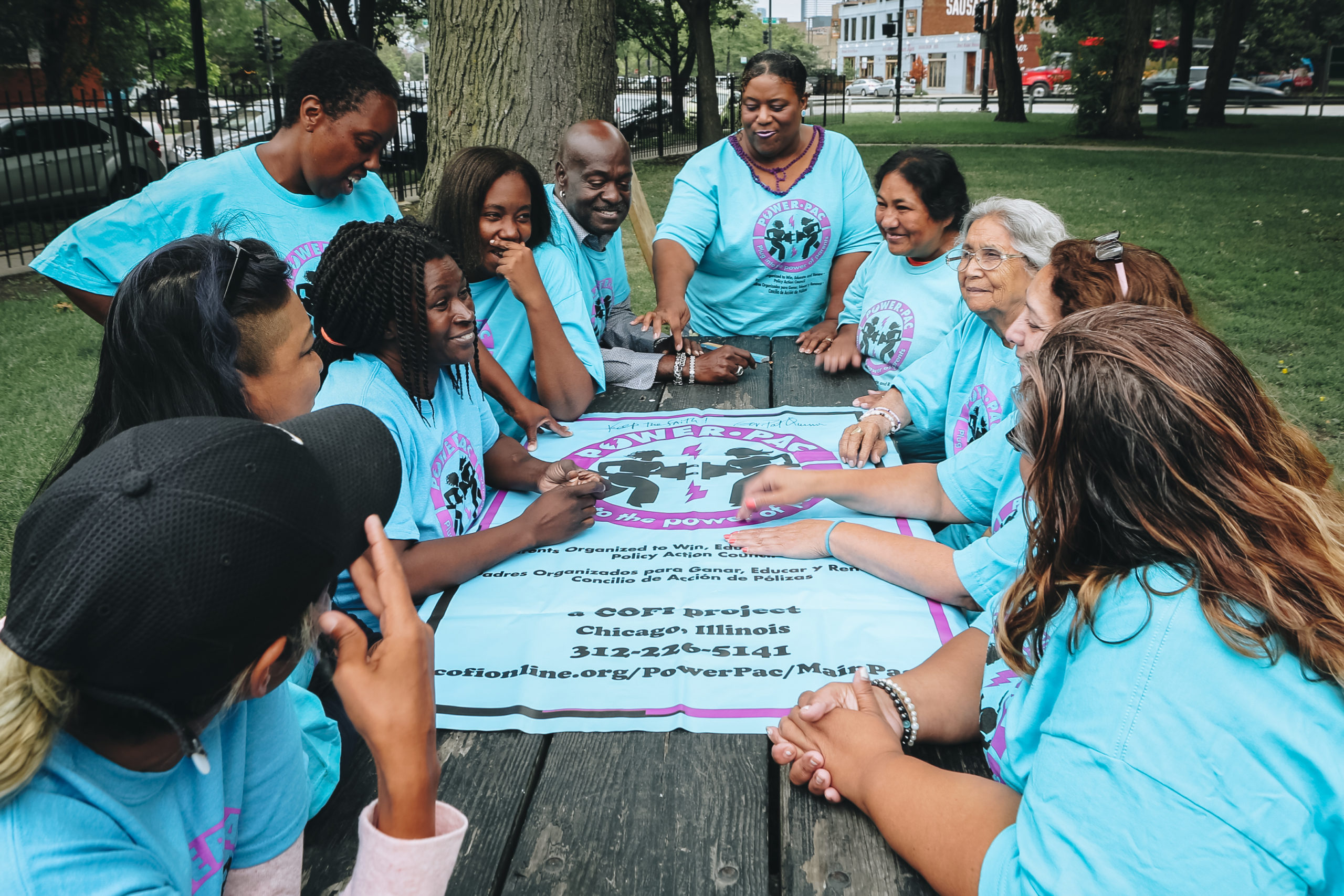 A group of parent leaders in matching blue shirts gather around a table , smiling at each other