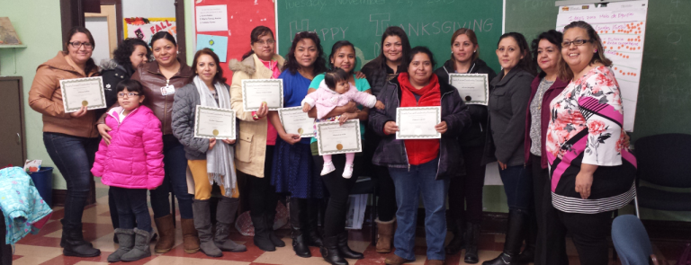 Un grupo de mujeres y niños latinos obtienen certificados para celebrar su graduación de la capacitación de COFI