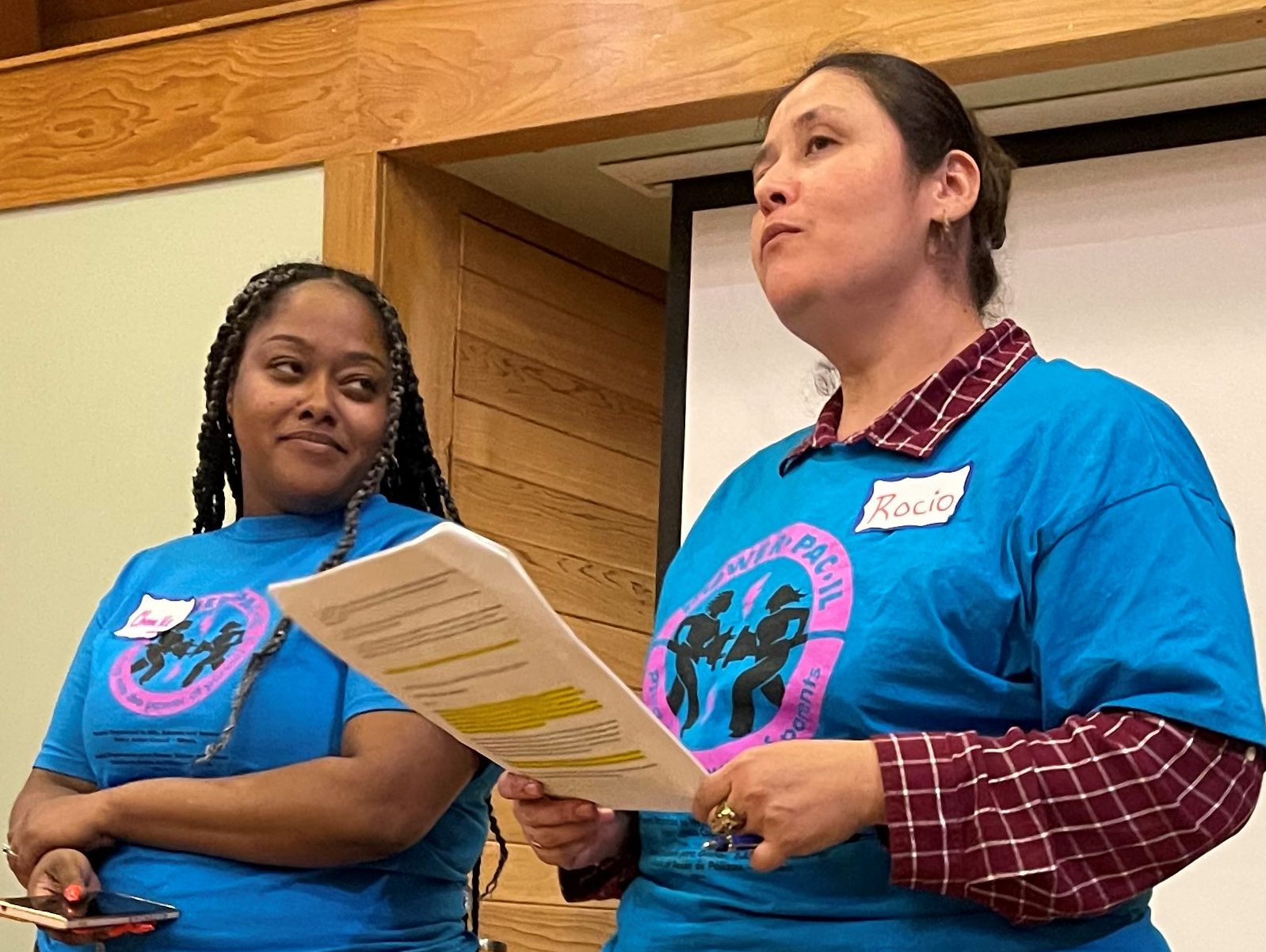 Dos mujeres con camisetas azules POWER-PAC IL a juego hablan en una reunión comunitaria a favor de la salud mental