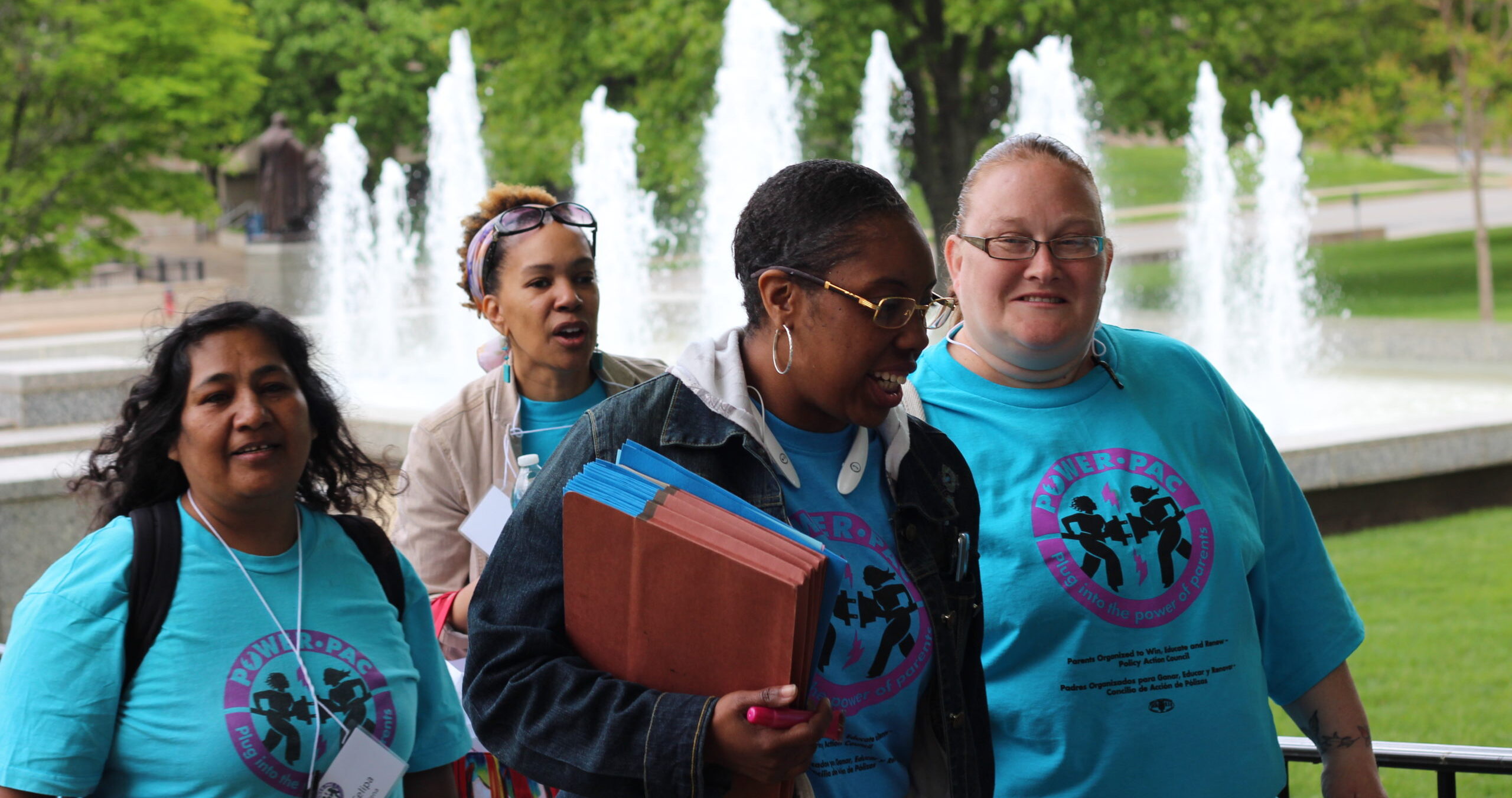 Four women, all wearing blue POWER-PAC IL shirts, walk outside the Illinois State Capitol