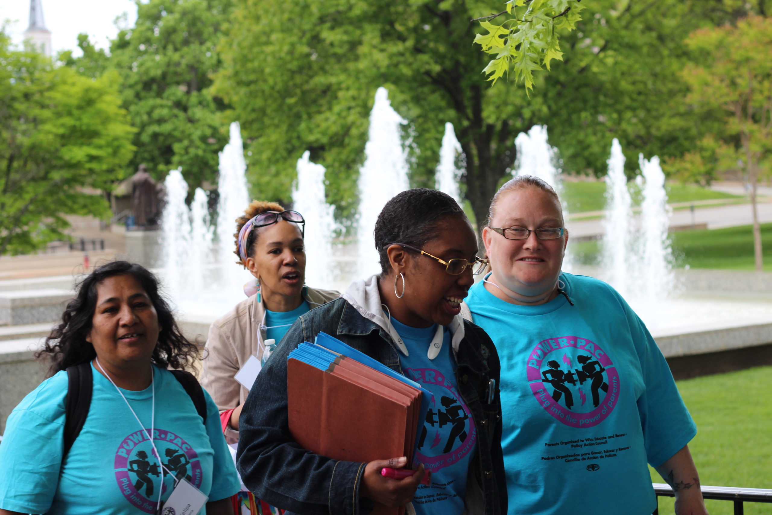 Cuatro mujeres, todas con camisetas azules POWER-PAC IL, caminan frente al capitolio del estado de Illinois