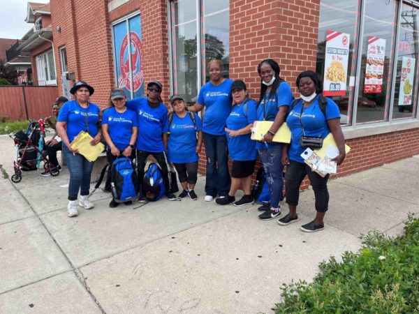 Eight people standing for a group picture; Some are holding backpacks or clipboards