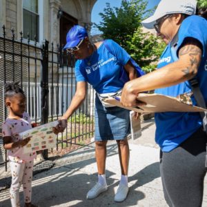 Two women give materials to a young girl while doing community outreach