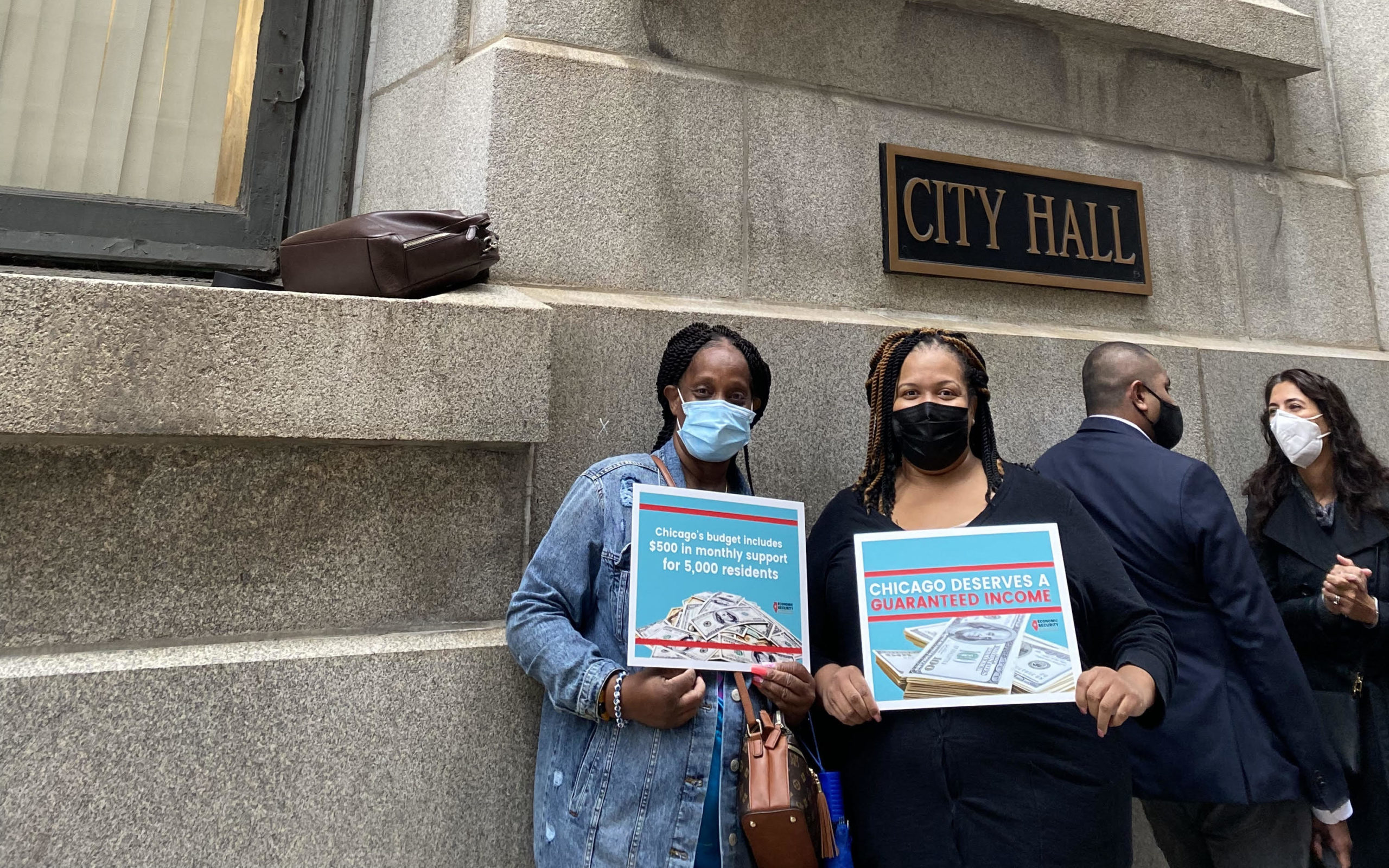 Dos mujeres en el ayuntamiento de Chicago con carteles que abogan por la Renta Garantizada