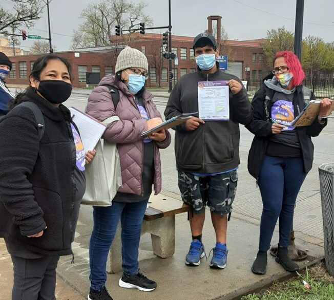 Four people stand by a Chicago bus stop with COVID vaccine materials for community outreach
