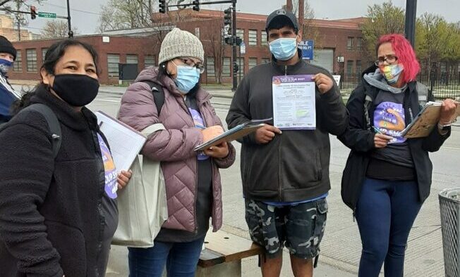 Four people stand by a Chicago bus stop with COVID vaccine materials for community outreach