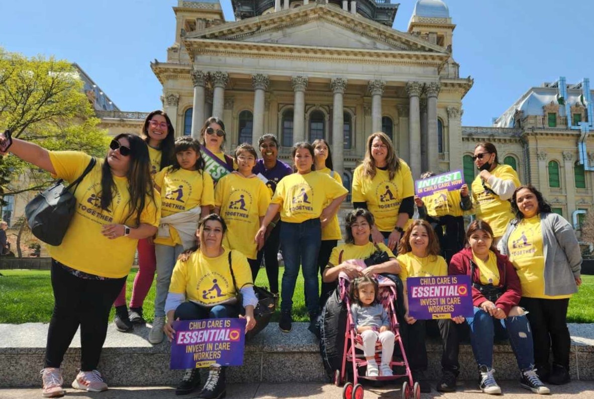 Un grupo de familias con camisas amarillas que abogan por la programación de la primera infancia se paran frente al Capitolio del Estado de Illinois