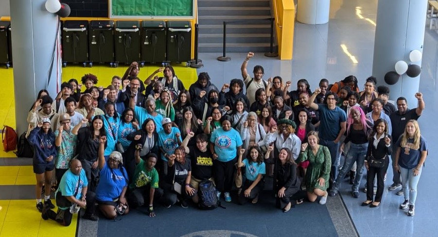 A large group photo of students, parents, CPS staff, and community members celebrating the expanded Whole School Safety policy. Many people have their fists in the air