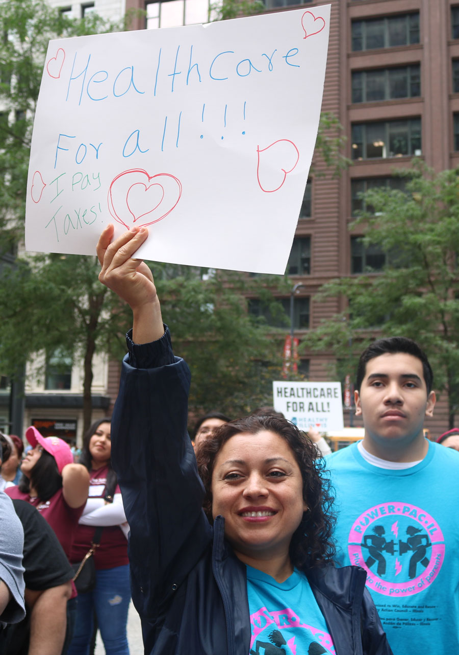 A Latina woman holds a sign that reads Healthcare for all