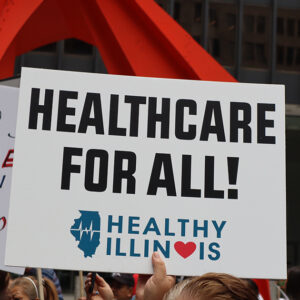 A picture of someone off-screen holding up a sign that reads "Healthcare for all!" from Healthy Illinois.