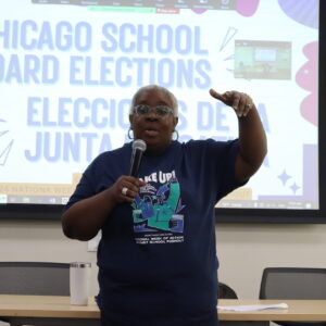 A Black woman speaking in front of a projector screen that says "Chicago School Board Elections"