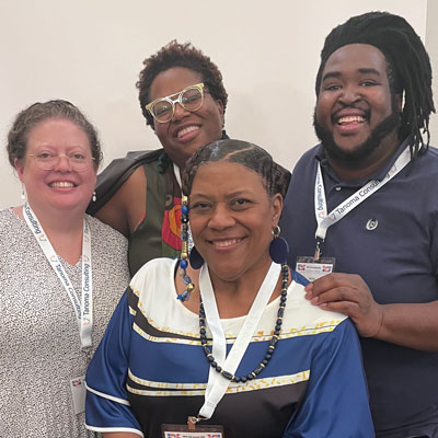 Ms Rose a Black woman with others at a conference - one White woman, a Black male, and Black woman