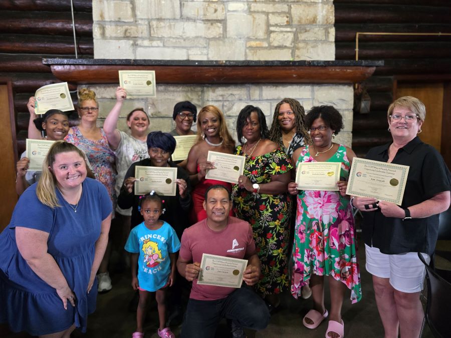 Una fotografía de la graduación de personas, familias y equipos de la Fase 1 de los Sistemas de Atención de Salud Mental para Jóvenes de Rockford. Hay alrededor de 12 adultos en la imagen y un niño.