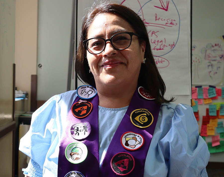 A Latina woman proudly shows off her purple sash covered with Advanced Leader badges